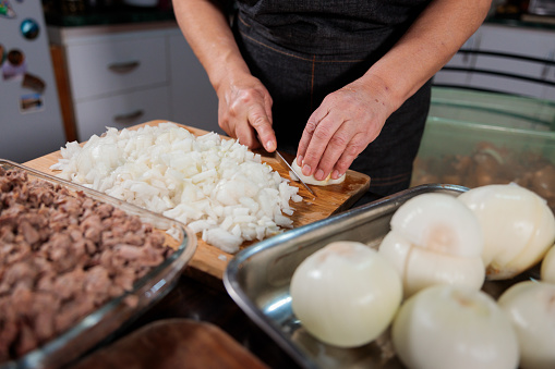 Close up of unrecognizable latin woman chopping onion and meat for filling chilean baked empanadas