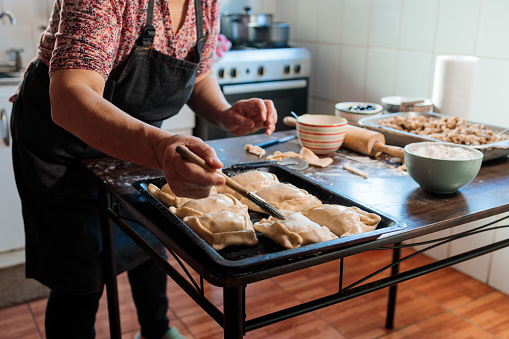 Traditional Chilean Cuisine: Unrecognizable Latina Woman Preparing a Tray of Baked Empanadas in Her Rustic Kitchen