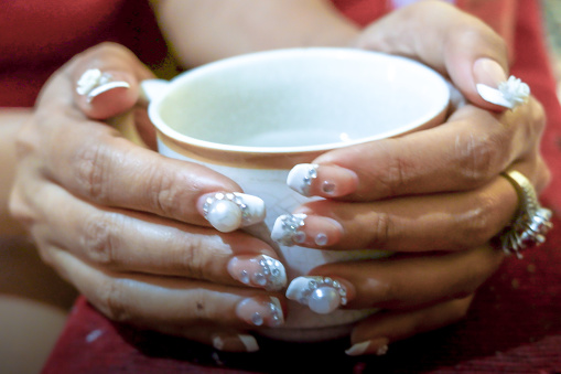 A woman with accessorized nails holds a cup.