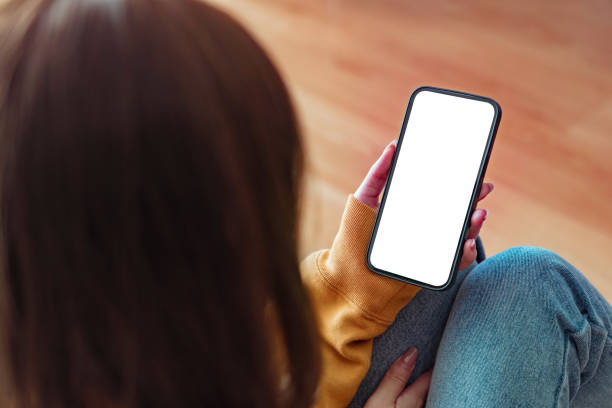 istock Hand holding mockup blank screen mobile smartphone on sofa at home, White empty space for advertise text. 1548793814