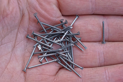 a pile of small gray metal nails lie on a brown palm on a hand