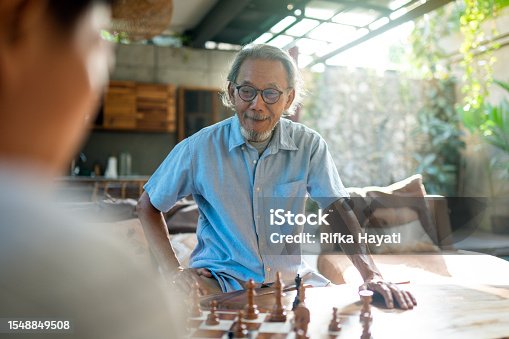 istock Asian senior man having fun with his friend by playing chess together at home. 1548849508
