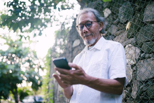 istock Happy asian senior man using mobile phone outdoor. 1548852701