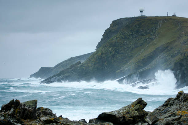 Big seas pound the huge black cliffs near Doolin, from waves that surge across the wild Atlantic Ocean, dwarfing an Irish mansion perched on the cliffs and glowing in the setting sun. The power of the rising seas is echoed in the frothy spume that coats the water's surface.