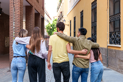 A heartwarming moment captured from behind, as five friends walk through a city street, their embrace exuding pure happiness and camaraderie.