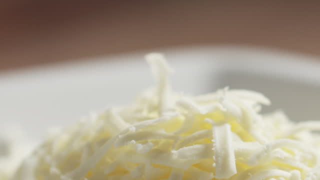 Slide shot of grated pizza mozzarella cheese falls in plate