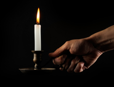 Hand holding a lit candle in the dark