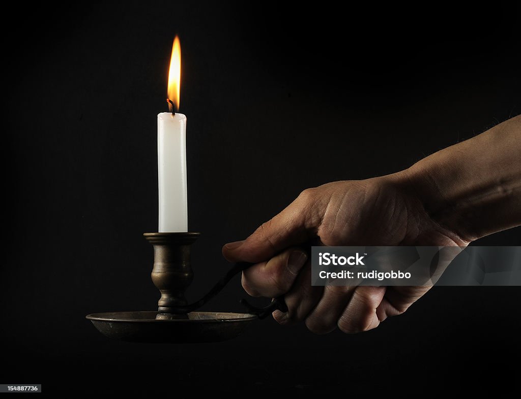 Hand holding a lit candle in the dark Holding a candleholder in the dark. Skin texture clearly visible. Blackout Stock Photo
