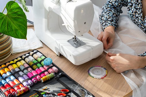 Woman hand close up sews tulle on electric sewing machine. Filling the thread into the sewing needle, adjusting the tension. Comfort in the house, a housewife's hobby, layout of sewing tools