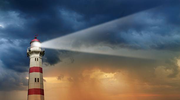 Lighthouse at dawn, bad weather in background Red and white striped partly sunlit lighthouse shining at dawn against a bad weather cloudscape. lighthouse stock pictures, royalty-free photos & images