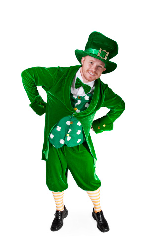 full length photograph of an adult man dressed in a leprechaun costume, standing with hands on waist, leaning and smiling directly at camera
