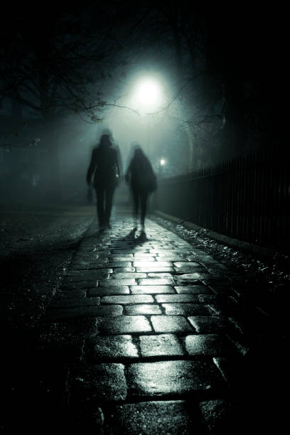 Two people walking down a dark alley in the evening fog