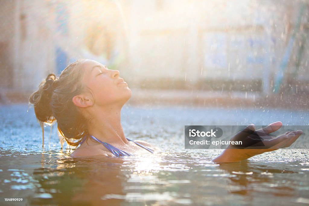 Young beautiful woman swimming in the rain Water droplets raining down on a woman in a swimming pool as the warm light of the setting sun hits her hands and face. Lake Stock Photo