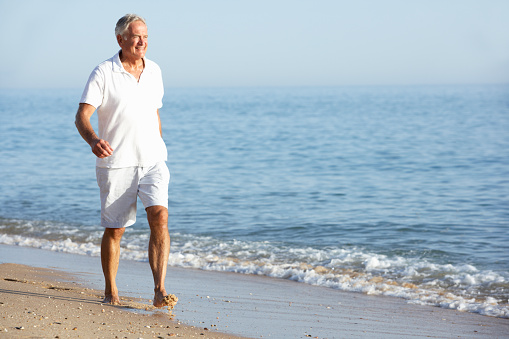 Senior Man Enjoying Beach Holiday Walking Along Seashore