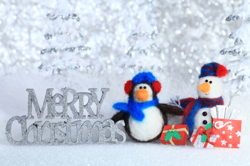XXXL photo - Christmas arrangement of a penguin, snowman and presents, with a glittered Merry Christmas text in front of snowy defocused trees and glitter.  The snowman and the penguin were made entirely from scratch by the photographer.  Selective focus on words.