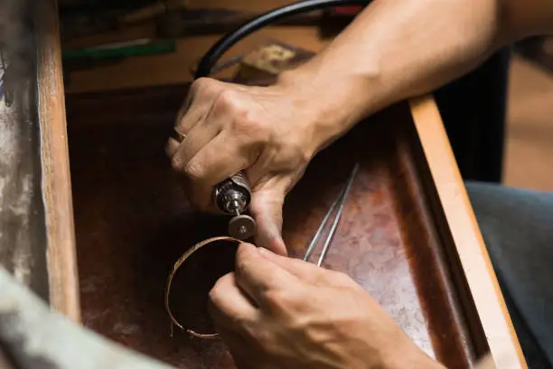 Photo of Close-up of a jeweler's hands polishing a gold bracelet.