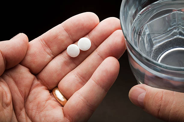 hands holding two aspirin and a glass of water . aspirin photos stock pictures, royalty-free photos & images