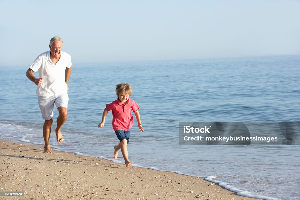 Grandfather And Grandson Running Along Beach Grandfather And Grandson Having Fun Running Along Beach Chasing Stock Photo