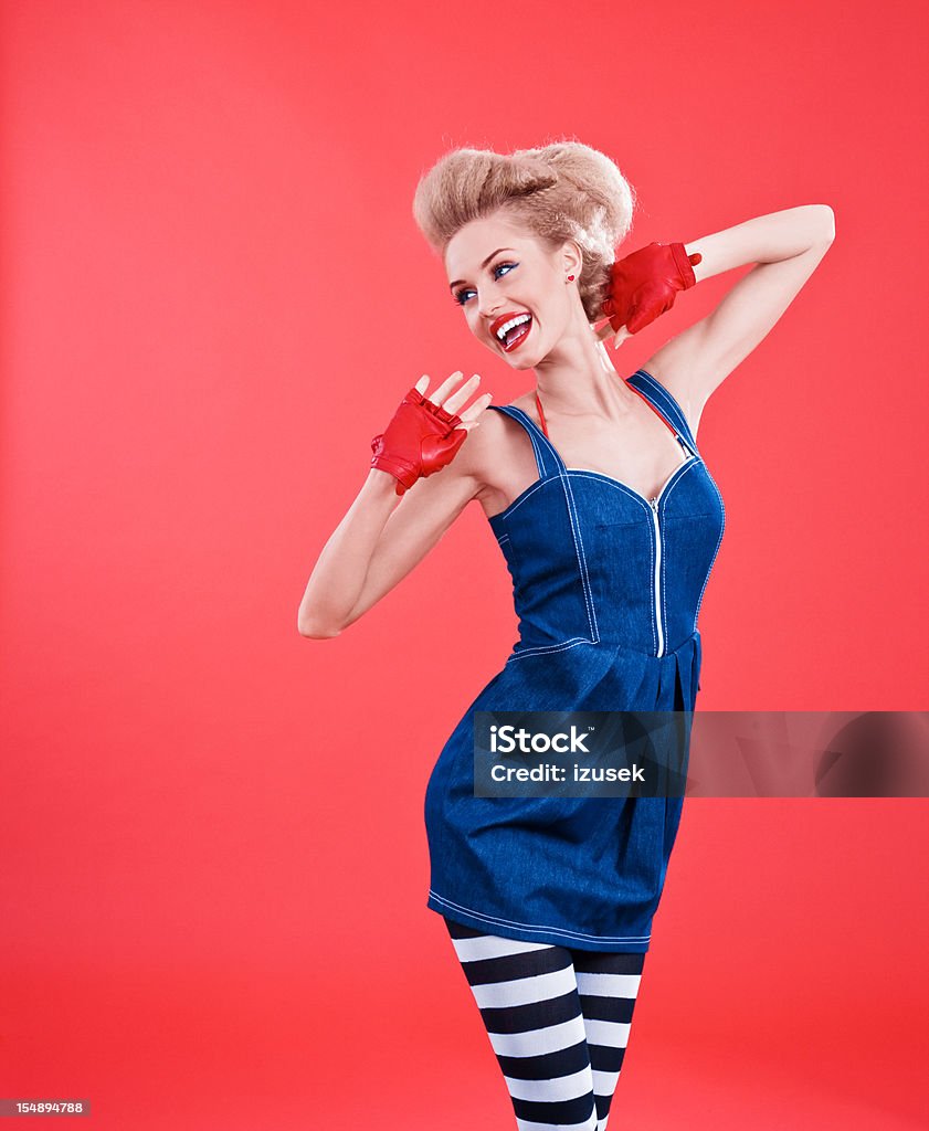 Fashion portrait of woman posing against red background Young blond beautiful woman wearing jeans dress, striped tights and red gloves posing against red background. Studio shot. One Woman Only Stock Photo
