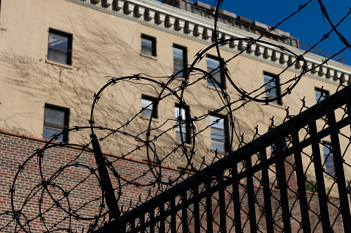 Looking up at a barbed wire fence in silhouette in front of an old brick apartment building in Brooklyn of New York City