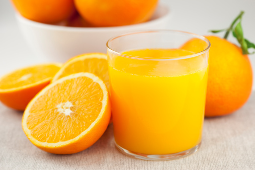 Glass of orange juice and oranges outdoors on a wooden table with nature background