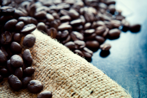 Aromatic coffee beans are displayed on a rustic burlap sack.  Macro shot with shallow depth of field.