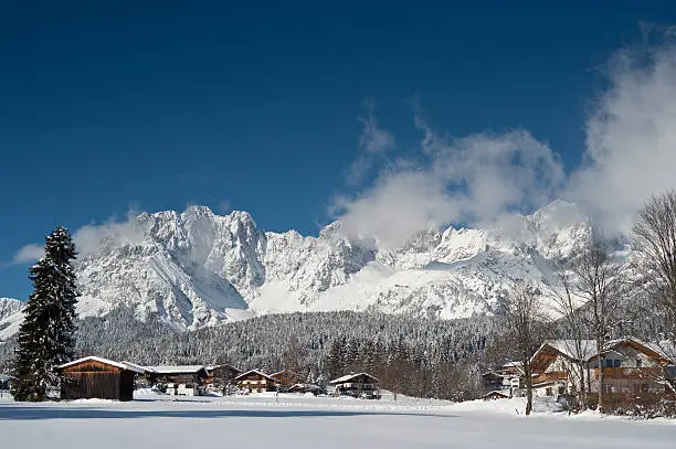 Beautiful mountain range called Wilder Kaiser at winter in Austria. Village of Going near Kitzbuehl, Tirol. Dark blue sky, winter wonderland, snowcapped peaks and fire trees.