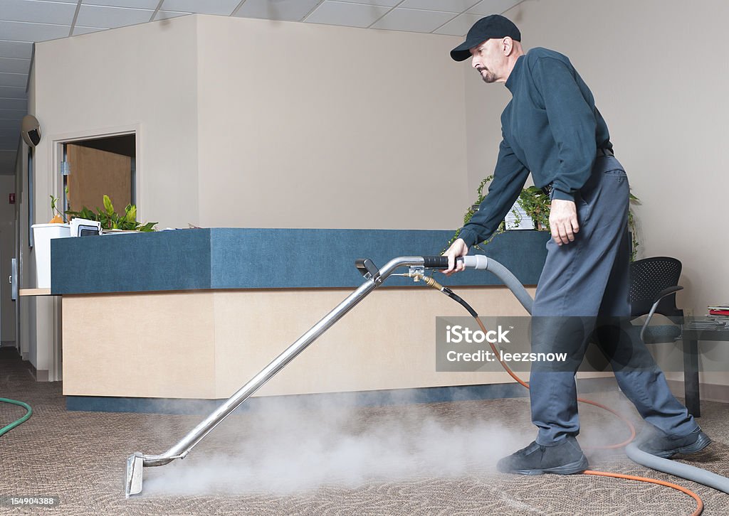 Professional Carpet Cleaner - Man Steam Cleaning Man steam cleaning the carpet of an office building.   Cleaning Stock Photo