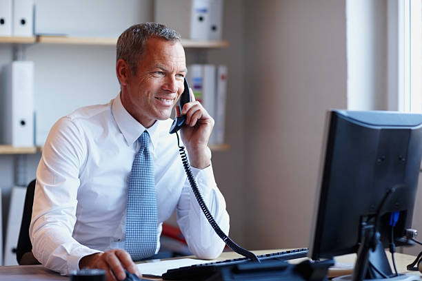 счастливый бизнесмен по телефону во время использования компьютера в офисе - necktie suit shirt business стоковые фото и изображения
