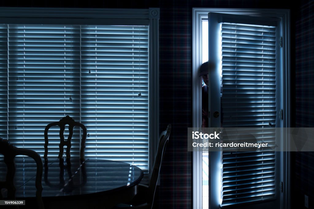 Burglar Breaking In To Home At Night Through Back Door This photo illustrates a burglary or thief breaking into a home at night through a back door. View from inside the residence. Thief Stock Photo