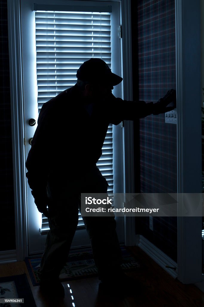 Shadow of man in the dark right next to the front door This photo illustrates a burglary or thief breaking into a home at night through a back door. View from inside the residence. Thief Stock Photo