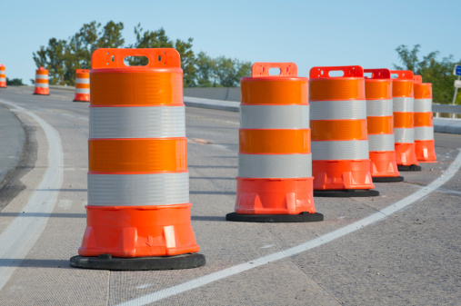 Orange barrels in highway construction zone as used in road maintenance and repair when creating traffic lane to guide drivers, summer morning side light, Pennsylvania, PA, USA.