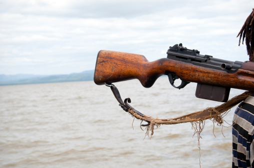 A rifle resting on the shoulder of a man beside Lake Chamo in Ethiopia