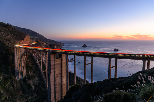 Light trails left by passing vehicles on Bixby Creek Bridge on the coast of central California at twilight in autumn. Big Sur, CA, USA.