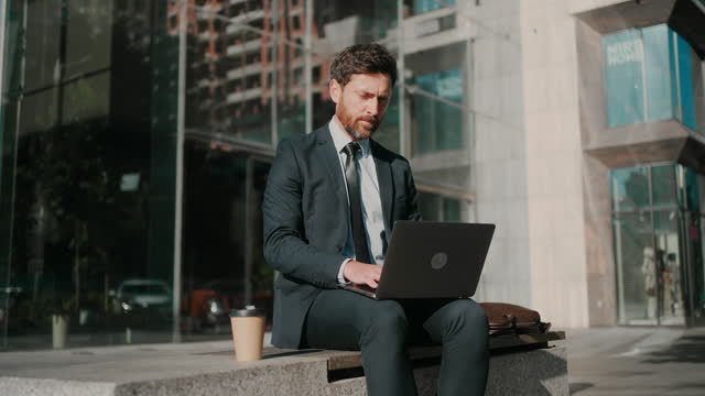 Man works on laptop sitting outside office in sunny morning
