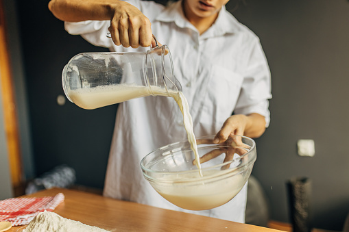 A young woman prepares dough, she pours milk into a glass container
