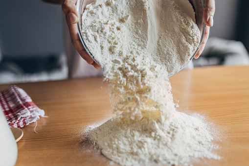 A woman spills the flour from the bowl onto the table and prepares to make the dough