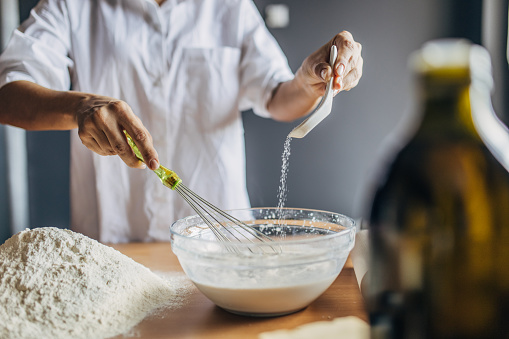 A young woman pours salt in a glass container with milk, she prepares the dough