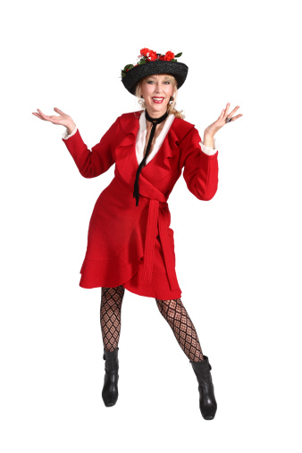 Vertical full length of smiling beautiful blond 50's woman wearing a red coat dress with a red flowered black straw hat. She's holding her arms up with graceful hands out to sides in a questioning gesture.
