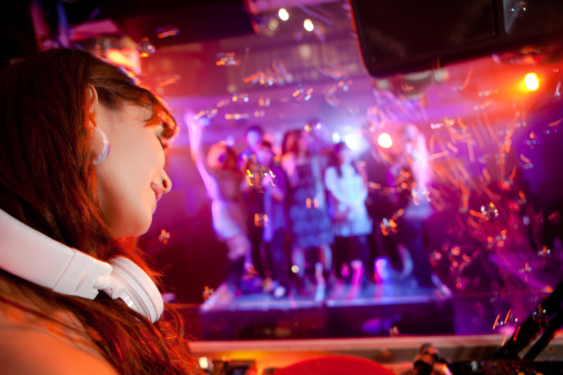 Female DJ in a nightclub with unrecognizable people in the background. 