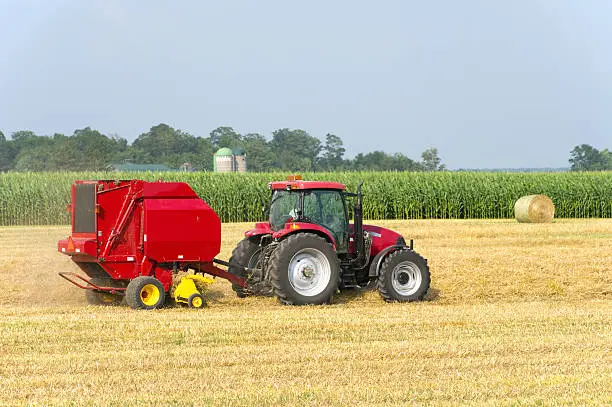 A large agricultural baler baling round bales of wheat straw.