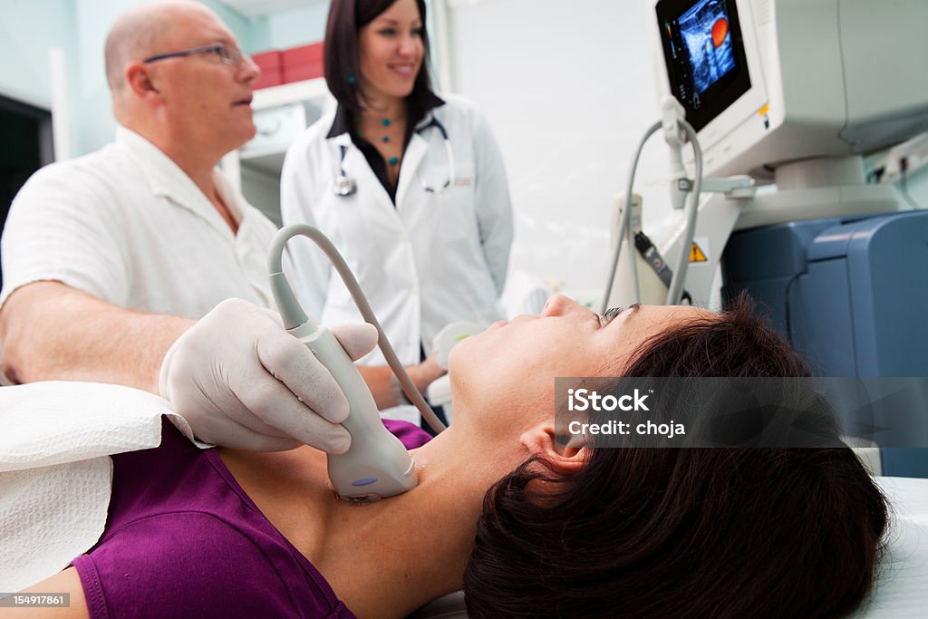 Doctor is giving beautiful young patient an ultra sound Doctor giving beautiful young patient an ultra sound of thyroid gland..trainee doctor is watching computer monitor   Color Image Stock Photo
