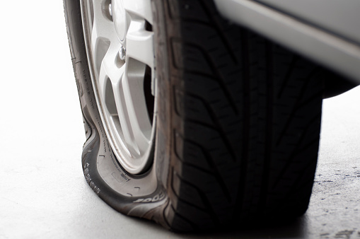 Flat tire on a passenger vehicle sitting on a garage floor, left side of image fades to white.