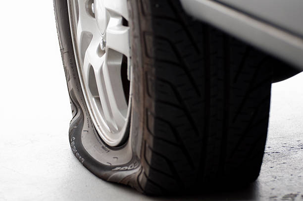 A flat tire is the focus isolated on white Flat tire on a passenger vehicle sitting on a garage floor, left side of image fades to white. flat tire stock pictures, royalty-free photos & images
