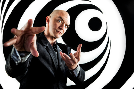 A hypnotist gesturing inducing a trance on a black and white swirl painted background.