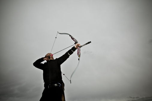 a male bow hunter draws back on his bow.