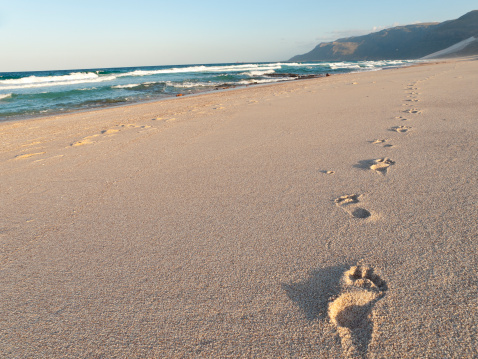 Footprints in wet sand on Margate ocean beach, South Africa. Blurred barefoot legs in the background in the distance. Vacation or holiday concept