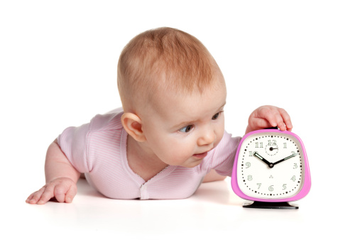 Portrait photograph of a 4 month baby girl and pink retro alarm clock.