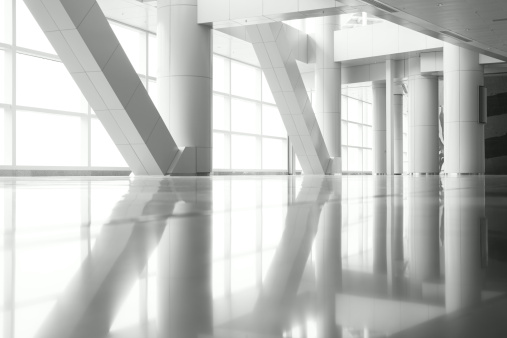 Light shining through the windows and columns of a modern architecture, with reflections on the floor.