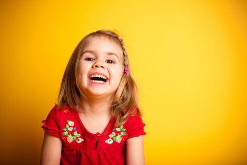 Color image of a little girl laughing while looking at the camera and isolated on yellow background. 
